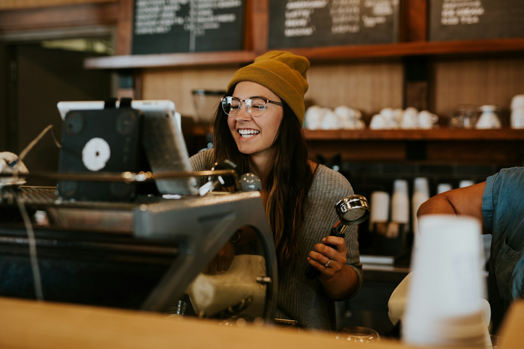 A smiling barista holding a portafilter behind the counter of her coffee shop.